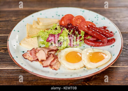 Englisches Frühstück mit frischen Salat. Englisches Frühstück - Spiegeleier, Speck und Würstchen, Toast, Tomaten und grünen Salat. appetitlichen Teller auf Pla Stockfoto