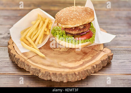 Hamburger mit frischem Gemüse und Fleisch. Burger mit Rindfleisch, Tomaten, Kopfsalat, eingelegte Gurken. cheesburger mit rustikalen Holzmöbeln Hintergrund. Stockfoto