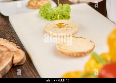 Der Prozess des Kochens Burger an Küche. bun für Hamburger gießen mit Soße. Kochen und kulinarisches Konzept. Stockfoto