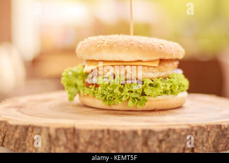 Chicken Burger mit Gemüse. Frischen appetitlichen cheesburger auf natürlichem Holz. klassische amerikanische Küche. Stockfoto