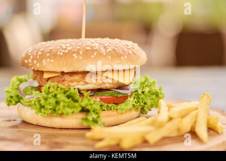 Appetitlich frischen Burger und Pommes frites. Huhn, Zwiebeln, Salat, Tomaten, Gurken, Käse Sandwich und gebratenen Kartoffeln. Stockfoto