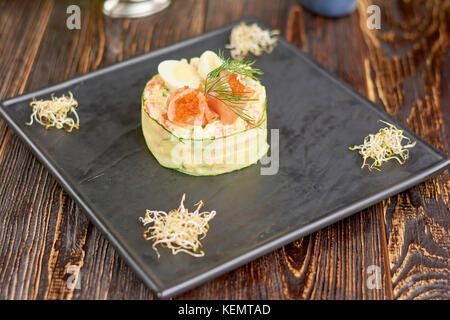 Olivier Salat mit Lachs und Tobiko Kaviar. appetitlich Olivier Salat auf Teller im Restaurant ein köstliches Abendessen auf dem Schwarzen Brett. Stockfoto