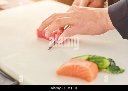 Koch schneiden frischer Thunfisch in kleine Stücke. Der Prozess der Schneiden roher Thunfisch Filet von Küchenchef. Küchenchef bei der Arbeit, Kochen. Stockfoto