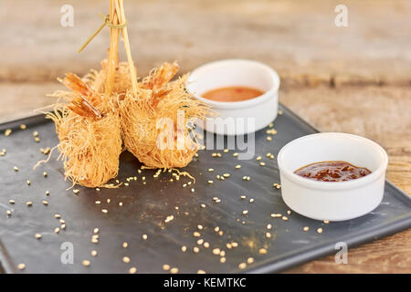 Garnelen eingewickelt in kataifi Teig an der Platte. appetitlich gebratene Garnelen in Teig kataifi mit Soße auf schwarze Platte serviert. knusprige Vorspeise im Restaurant. Stockfoto