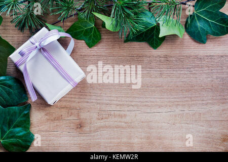 Grenze von Efeu Blätter und Zweige Tannenbaum, mit rustikalen Weihnachtsgeschenke auf abstrakte Holz- Hintergrund. nach oben anzeigen und Platz für Text. Stockfoto