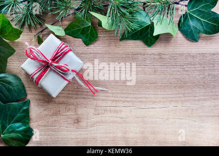 Grenze von Efeu Blätter und Zweige Tannenbaum, mit rustikalen Weihnachtsgeschenke auf abstrakte Holz- Hintergrund. nach oben anzeigen und Platz für Text. Stockfoto