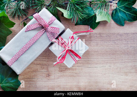 Grenze von Efeu Blätter und Zweige Tannenbaum, mit rustikalen Weihnachtsgeschenke auf abstrakte Holz- Hintergrund. nach oben anzeigen und Platz für Text. Stockfoto