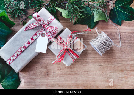 Grenze von Efeu Blätter und Zweige Tannenbaum, mit rustikalen Weihnachtsgeschenke auf abstrakte Holz- Hintergrund. nach oben anzeigen und Platz für Text. Stockfoto