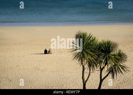 Ein Paar, das in der ruhigen Umgebung von Sand und Meer an der Carbis Bay in der Nähe von St Ives, Cornwall entspannen Stockfoto