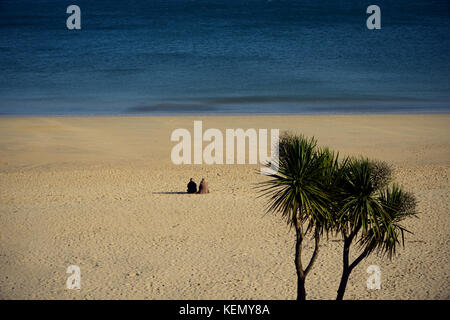 Ein Paar, das in der ruhigen Umgebung von Sand und Meer an der Carbis Bay in der Nähe von St Ives, Cornwall entspannen Stockfoto