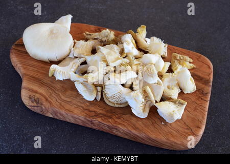 Frische Austernpilze in grosse Stücke auf einem olivenholz Schneidbrett auf einem grauen Abstrakt Hintergrund ausschneiden. Schritt für Schritt kochen Stockfoto