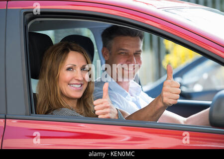 Gerne älteres Ehepaar sitzt im neuen Auto und zeigen Daumen hoch Stockfoto
