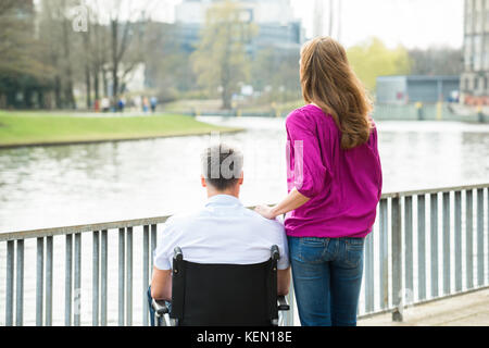 Rückansicht der Frau mit Ihren behinderten Mann im Rollstuhl auf See Stockfoto