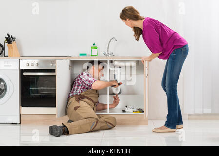 Männliche Klempner Instandsetzung Rohr unter der Spüle, während Frau steht in der Küche Stockfoto