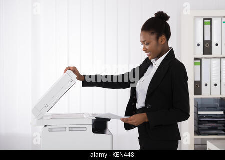 Lächelnden jungen afrikanischen Geschäftsfrau Einlegen von Papier für Kopierer im Büro Stockfoto