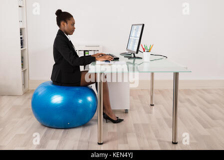 Junge afrikanische Geschäftsfrau mit Computer sitzend auf Fitness Ball im Büro Stockfoto