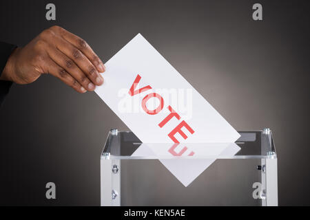 Nahaufnahme einer Person hand Abstimmung in einer Wahlurne gegen grauer Hintergrund Stockfoto