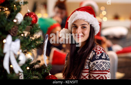 Urlaub, Winter und Personen Konzept - glückliche junge Frau in Santa Hut von Weihnachtsbaum zu Hause Stockfoto