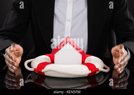 Nahaufnahme der Hand Kaufmann schutz Haus Modell mit Rettungsring auf Schreibtisch Stockfoto