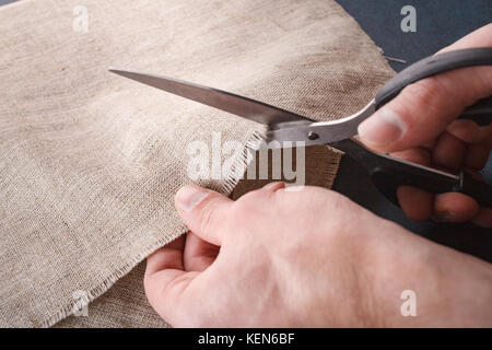 Hand schneidet ein Leinentuch mit der Schere zuschneiden. Stockfoto