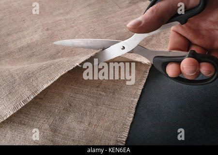 Hand schneidet ein Leinentuch mit der Schere zuschneiden. Stockfoto