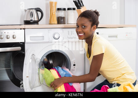 Junge afrikanische Frau, die Kleidung in die Waschmaschine zu Hause Stockfoto