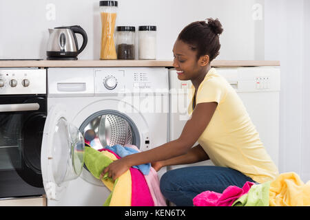 Junge afrikanische Frau, die Kleidung in die Waschmaschine zu Hause Stockfoto