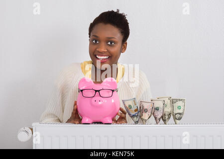 Porträt eines lächelnden jungen afrikanischen Frau mit Sparschwein in der Nähe von Banknoten Stockfoto