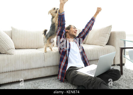 Happy Guy frohlockt mit seinem Hund sitzt in der Nähe der Couch im Wohnzimmer. Stockfoto
