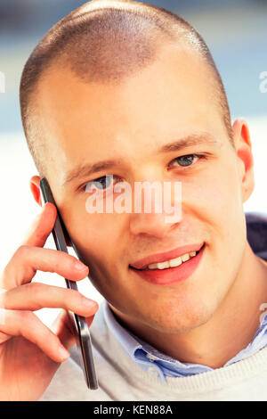 Nahaufnahme, Porträt einer fröhlichen hübscher junger Mann am Telefon sprechen und lächelnd, während man im Freien Stockfoto