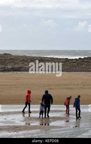 Eine große Familie zu Fuß auf einem windigen Strand zwischen Felsen und im Sand Rock Pools an der Bude auf der Nordküste von Cornwall Küste paddeln nasse Füße. Stockfoto