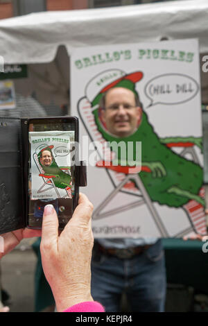 Eine Frau braucht ein Handy Foto von ihrem Ehemann bei der jährlichen Essiggurke Tag Feier auf der Orchard Street auf der Lower East Side von Manhattan. Stockfoto