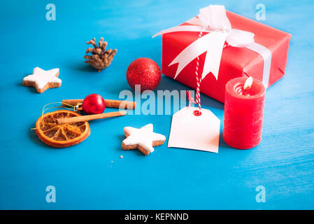 Geschenk verpackt in rotem Papier und mit weißem Band und Bogen gebunden, mit einem leeren Etikett befestigt ist, durch die sternförmige Cookies, Gewürze, Globen umgeben, ein Stockfoto