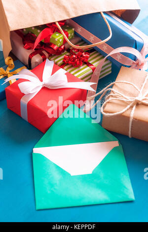 Fröhliches Bild mit grünem Umschlag mit leerem Papier von mehrfarbigen präsentiert umgeben, die aus einem umgestürzten Shopping Bag kam. Stockfoto