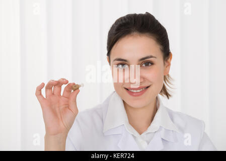 Porträt der glückliche junge Ärztin holding Hörgerät Stockfoto