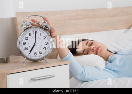 Junge Frau ausschalten Alarm beim Schlafen auf dem Bett Stockfoto
