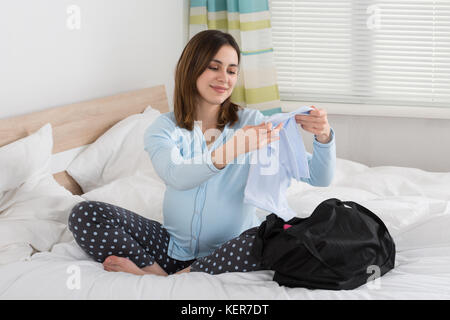 Schwangere Frau sitzt auf dem Bett, baby Tuch suchen Stockfoto