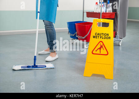 In der Nähe der weiblichen Hausmeister wischen Flur mit Warnschild Stockfoto