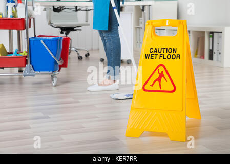 In der Nähe der weiblichen Hausmeister wischen Holzboden mit Warnschild Stockfoto