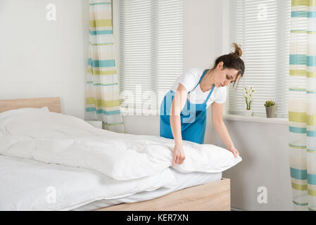 Junge weibliche Haushälterin, die die Bettlaken auf dem Bett im Zimmer Stockfoto