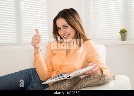 Gerne Frau sitzt auf einem Sofa Gestik, die Daumen hoch halten Tagebuch Stockfoto