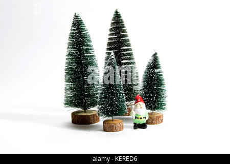 Isolierte Gruppe der vollen künstliche Tannen wie ein kleiner Wald Baum mit einer Figur von gartenzwerg innen auf einem weißen Hintergrund. Minimale still life Foto Stockfoto