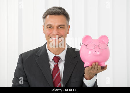 Reifen glücklich Geschäftsmann holding Sparschwein im Büro Stockfoto