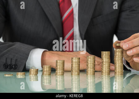 Nahaufnahme der Geschäftsmann Hand Münze über Stapel von Münzen am Schreibtisch Stockfoto