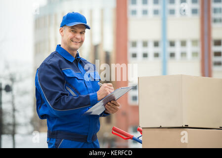 Portrait von zuversichtlich Delivery Man mit Paketen und Zwischenablage gegen Lkw Stockfoto