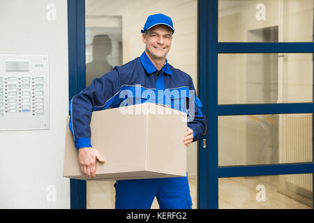 Reifen glücklich deliveryman stehen in der Nähe der Tür Holding Box Stockfoto