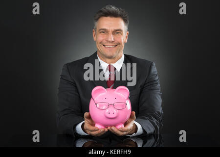 Reifen gerne Unternehmer sitzen und halten Sparschwein Stockfoto