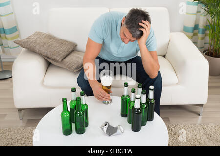 Reifen Mann sitzt auf einem Sofa Vor der Flasche Bier auf Tisch Stockfoto