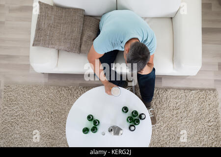 Reifen Mann sitzt auf einem Sofa Holding Glas Voller Bier zu Hause Stockfoto