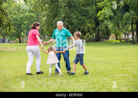 Gerne ältere Großeltern und Enkel halten einander die Hände beim Spielen im Park Stockfoto